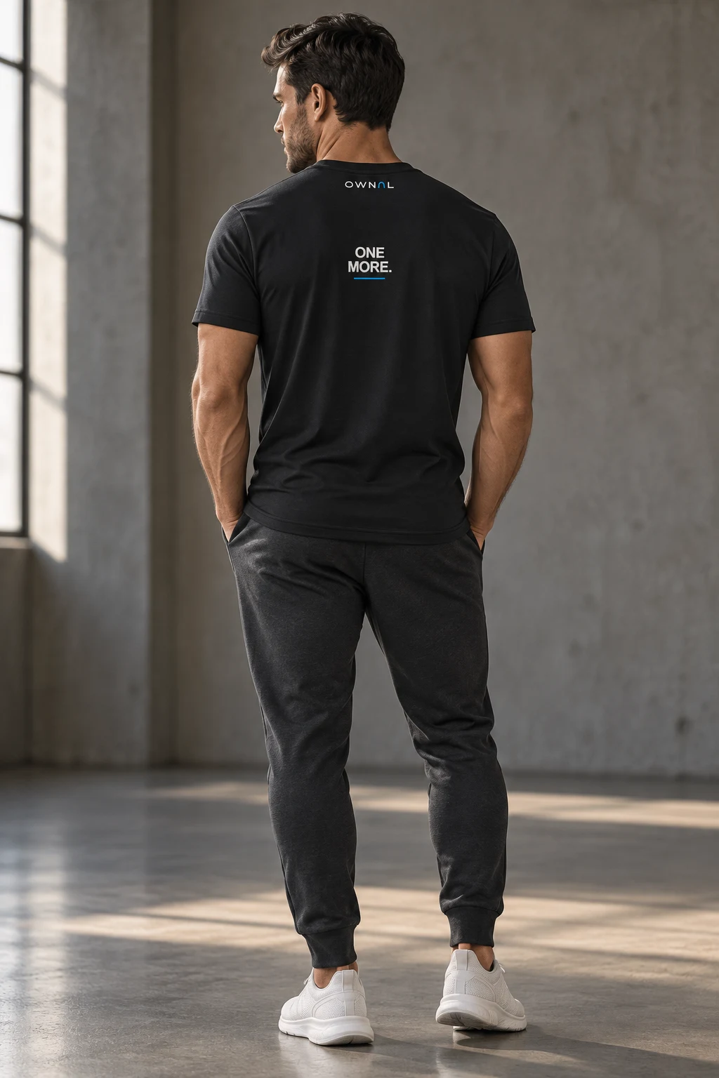 Male model in a black OWNAL tee with a small ONE MORE upper-back print and graphite joggers
